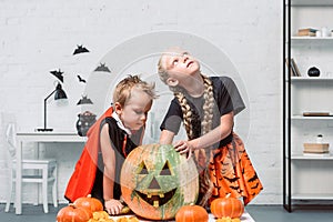 little kids in halloween costumes near table with pumpkins