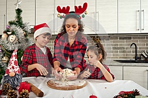 Little kids helping their mom to knead a dough on a wooden board, cooking at home kitchen for Christmas traditional events.