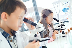 Little kids learning chemistry in school laboratory looking in microscopes