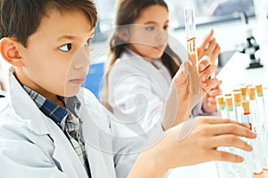 Little kids learning chemistry in school laboratory looking on test tubes