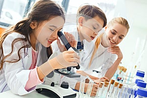 Little kids with teacher in school laboratory looking in microscope