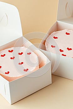 Little Korean style pink bento cake with hearts in a white box on the beige background. Pastry as a gift for a birthday of