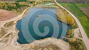 Little lake or pond of unusual shape with a beautiful autumn nature and gravel piles photographed from above with a drone.