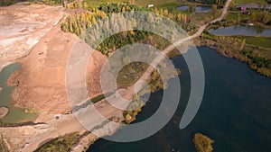 Little lake or pond of unusual shape with a beautiful autumn nature and gravel piles photographed from above with a drone.