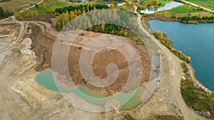 Little lake or pond of unusual shape with a beautiful autumn nature and gravel piles photographed from above with a drone.