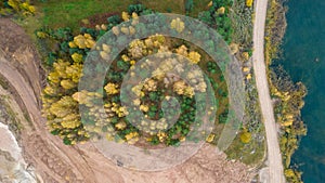 Little lake or pond of unusual shape with a beautiful autumn nature and gravel piles photographed from above with a drone.