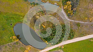 Little lake or pond of unusual shape with a beautiful autumn nature and mud road photographed from above with a drone.