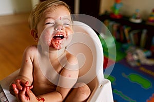 Little laughing baby with dirty face sits on a chair, arms folded