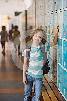 Little learner standing near lockers in school hallway