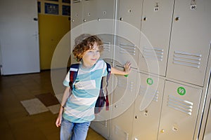 Little learner standing near lockers in school hallway