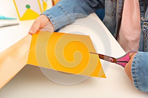 Little left-handed girl cutting orange construction paper at table