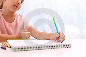 Little left-handed girl drawing at table in room