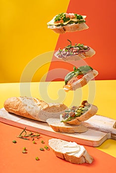 Little levitating baguette sandwiches on vibrant yellow and orange background decorated with greens