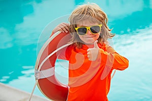 Little lifeguard show thumb up, ok. Summer kids holidays. Happy child playing with lifebuoy in the sea. Kids having fun