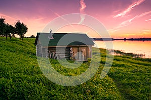 Little lone house on banks of the river at sunset in silence