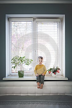 Little loneliness kid boy sitting on windowsill