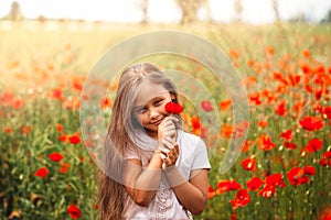 Little longhaired girl  posing at field of poppies with  on summer sun