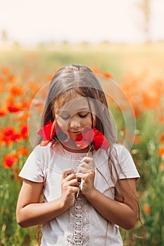 Little longhaired girl  posing at field of poppies with  on summer sun. Vertical