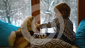 Little lovely blond boy is touching the nose of his fluffy pomeranian spitz. Cute dog is licking the toodler while