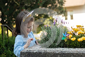 Little lovely girl with a crown happy birthday on her head and in a denim blue dress looks at a lavender flower