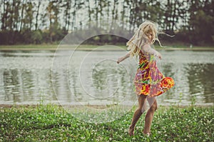 Little lovely girl dancing in the grass by the river