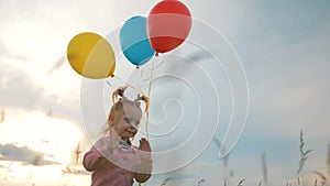 A little lovely girl, a happy child running on the green grass with colorful balloons in her hands. The concept of