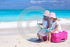 Little lovely girls sitting on big suitcase and a map at tropical beach