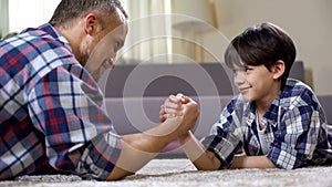Little male kid challenging his father in arm wrestling, having fun together