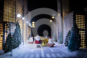 Little miniature city with road and lights. Decorative cute small houses in snow at night in winter. Creative Holiday concept.