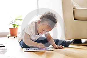 Little mixed-race girl at home playing game on tablet.