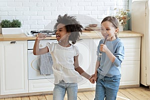 Little mixed race preschool kids enjoying singing songs in kitchen.