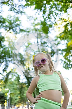 Little model girl posing at the camera in sunglasses, holding her hand on her hips