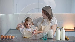 Little mothers helper. Small girl going to beat the dough for pancakes. Mom teach daughter to cook.