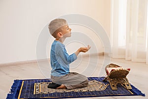 Little Muslim boy with Koran praying on rug