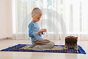 Little Muslim boy with misbaha and Koran praying on rug