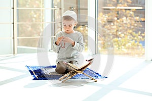 Little Muslim boy with misbaha and Koran praying on rug