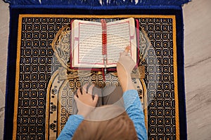 Little Muslim boy reading Koran on prayer rug