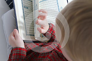 Little muslim European boy with islamic holy book Quran or Kuran