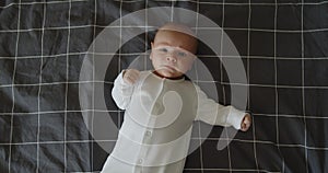 Little newborn baby boy lies on a bed on his back crying looking at camera