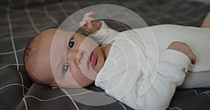 Little newborn baby boy lies on a bed on his back looking at camera