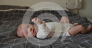 Little newborn baby boy lies on a bed on his back looking at camera