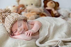 Little newborn baby boy, sleeping with teddy bear at home in bed