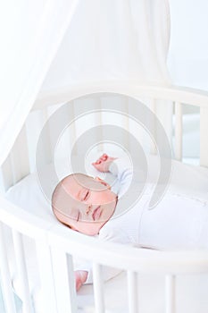 Little newborn baby boy sleeping in white round crib