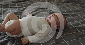 Little newborn baby boy yawns while lying on a bed on his back at home