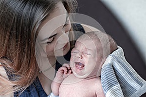 A little newborn baby is crying in his mother`s arms