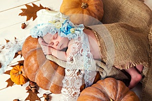 Little newborn baby girl in a lace bonnet like Cinderella sleeping on a pumpkin