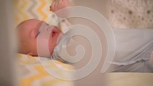 Little newborn baby lies in a crib and nibbles a toy