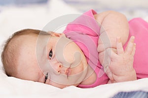 Little newborn lying on her stomach on a white bed. The newborn is awake looking around in the room. Newborn baby in a