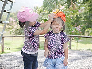 Little older sister, 3 years old, putting on her lovely younger sister, 2 years old, a cap - sisters love / care / bond
