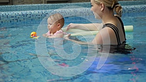 A little one-year-old girl learns to swim with her mother in the pool.